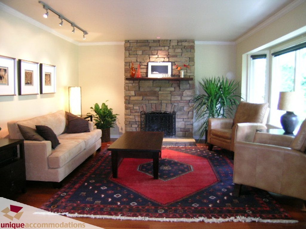 Furnished living room with stone fireplace, hardwood floors, and a red patterned rug. - 1385 East 15th Street, North Vancouver