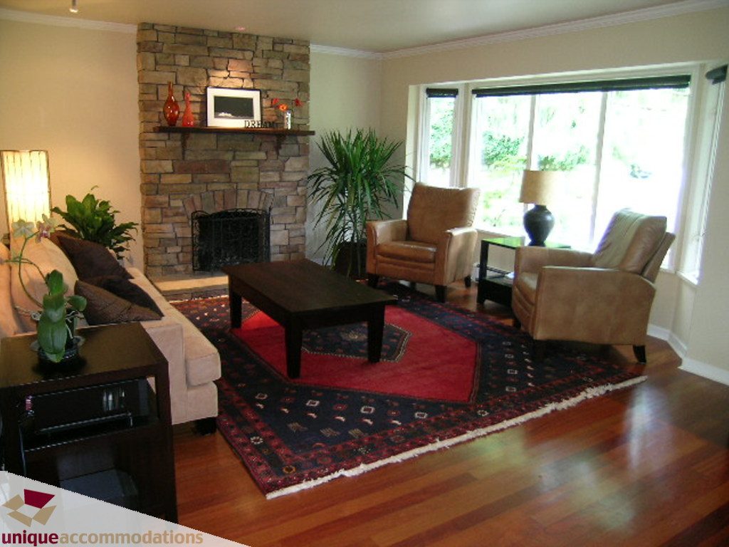 Furnished living room with hardwood floors, stone fireplace, and large windows. - 1385 East 15th Street, North Vancouver