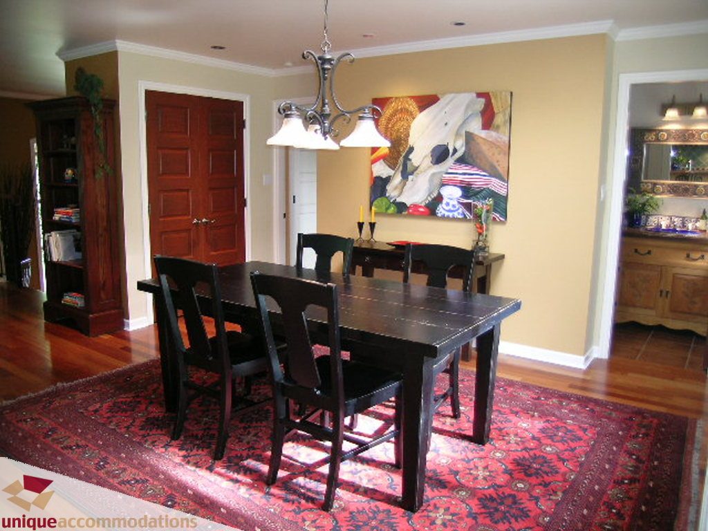 Furnished dining room with hardwood floors, dark wood table, and red patterned rug. - 1385 East 15th Street, North Vancouver