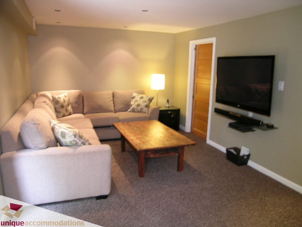 Furnished living room with a large sectional sofa, wooden coffee table, and flat-screen TV mounted on the wall.
