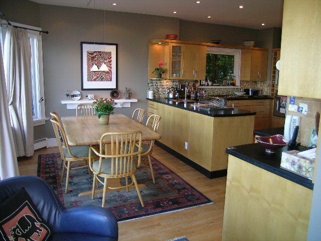 Open kitchen and dining area with wooden cabinets, black countertops, and hardwood floors. - 4663 Bellevue Drive, Vancouver West Side