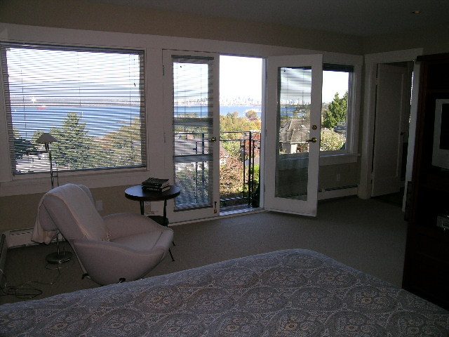 Bright bedroom with large windows offering a city view, furnished with a bed and chair. - 4663 Bellevue Drive, Vancouver West Side