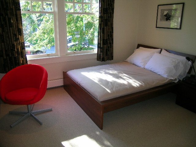Bright bedroom with modern furniture, red chair, and large window view. - 4663 Bellevue Drive, Vancouver West Side
