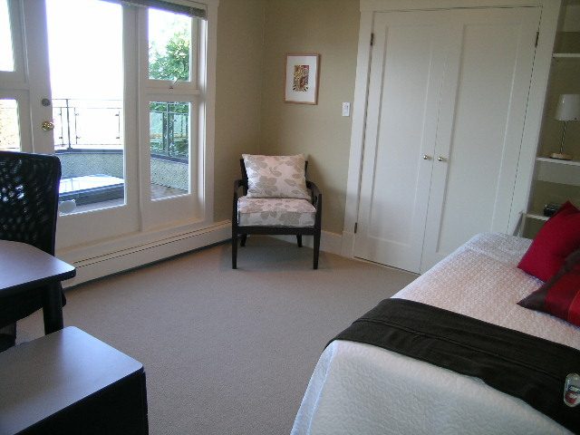 Spacious bedroom with large windows, cozy seating, and neatly made bed with red pillows. - 4663 Bellevue Drive, Vancouver West Side