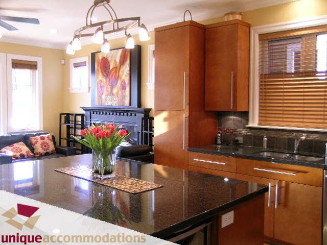 Bright kitchen with granite countertops and modern cabinetry, open to a living area with a floral painting.