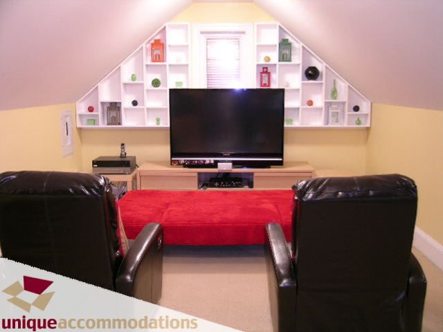 Bright living room with a large TV, red accent furniture, and white shelving. - 3030 West 15th Avenue, Vancouver West Side