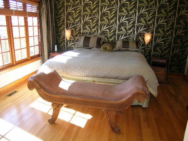 Spacious bedroom with wooden floors, patterned wallpaper, and a cozy bed setup. - 2148 Kings Ave, West Vancouver