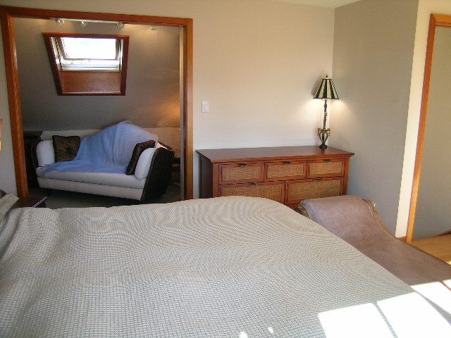 Cozy bedroom with a bed, nightstand, and lamp; large window above the couch. - 2148 Kings Ave, West Vancouver