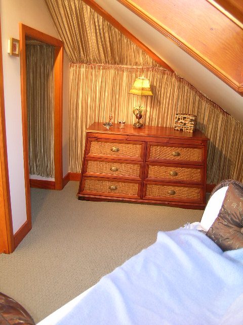 Cozy attic bedroom with wooden dresser, wicker drawers, and striped curtains. - 2148 Kings Ave, West Vancouver