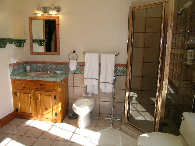 Bright bathroom with wooden cabinets, tiled countertop, and large mirror. - 2148 Kings Ave, West Vancouver