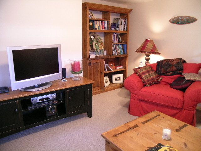 Living room with red couch, wooden bookshelf, and flat-screen TV. - 2148 Kings Ave, West Vancouver