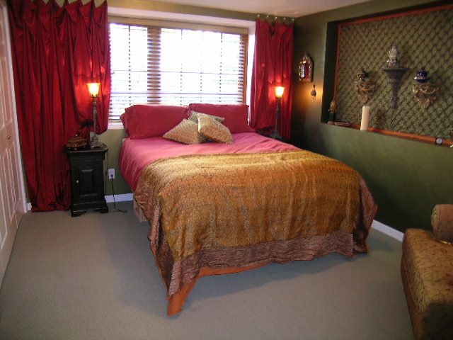 Spacious bedroom with red curtains, patterned bedding, and wall-mounted decor. - 2148 Kings Ave, West Vancouver