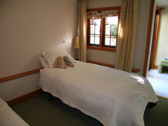 Bright bedroom with white bedding, wooden trim, and a window with curtains. - 2148 Kings Ave, West Vancouver
