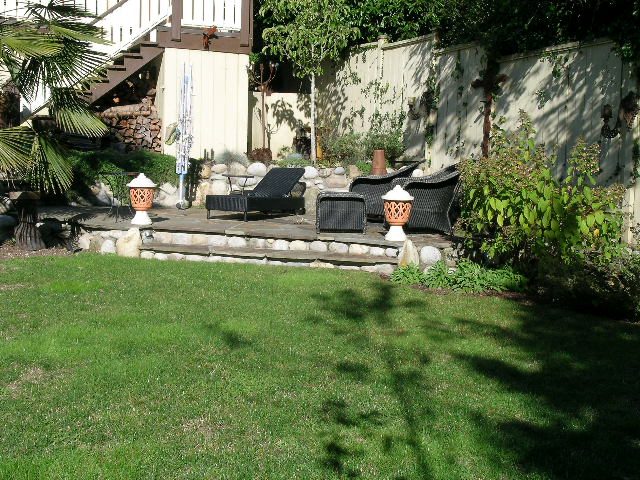 Spacious backyard with lush green lawn, patio furniture, and privacy wall. - 2148 Kings Ave, West Vancouver