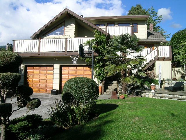 Bright living room with large windows and a cozy fireplace, surrounded by lush greenery. - 2148 Kings Ave, West Vancouver