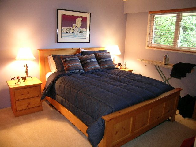 Spacious bedroom with wooden furniture, blue bedding, and a window with blinds. - 875 Whitchurch Street, North Vancouver