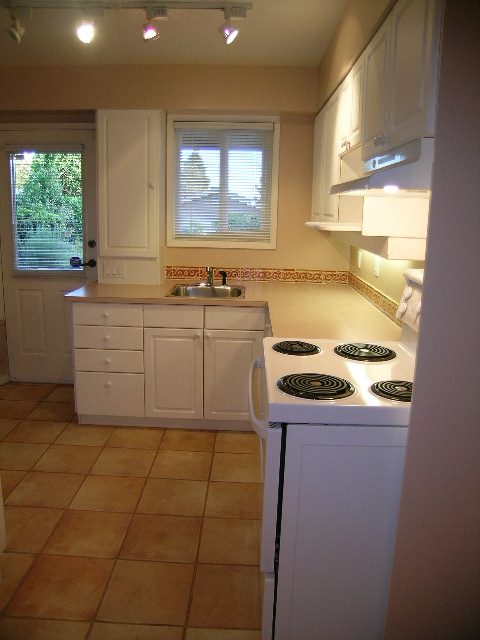 Bright kitchen with white cabinets, tile countertops, and a view of greenery outside. - 875 Whitchurch Street, North Vancouver