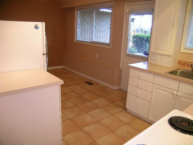 Bright kitchen with white cabinets, tiled floor, and natural light from windows. - 875 Whitchurch Street, North Vancouver