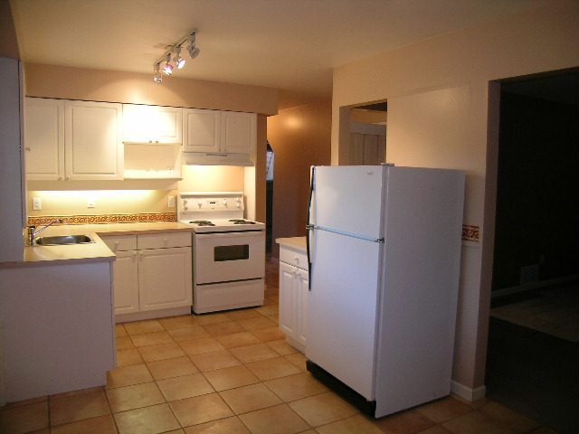 Bright kitchen with white cabinets, tiled floor, and a view into the living area. - 875 Whitchurch Street, North Vancouver