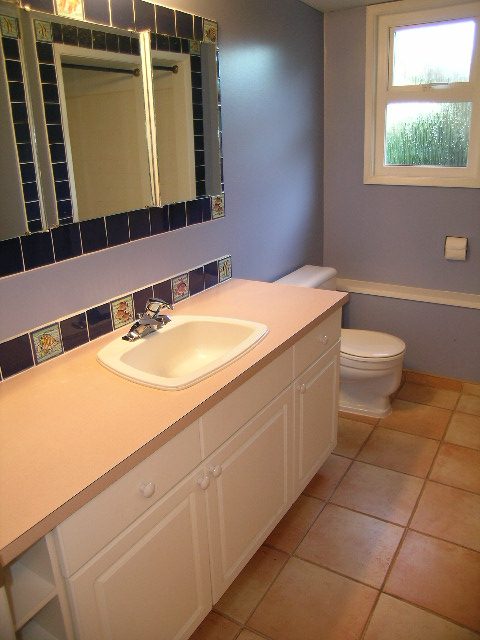 Bright bathroom with white cabinets, beige countertop, and tiled backsplash. - 875 Whitchurch Street, North Vancouver