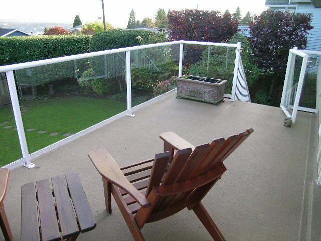 Deck with wooden chairs and glass railings, overlooking a green lawn and trees. - 875 Whitchurch Street, North Vancouver