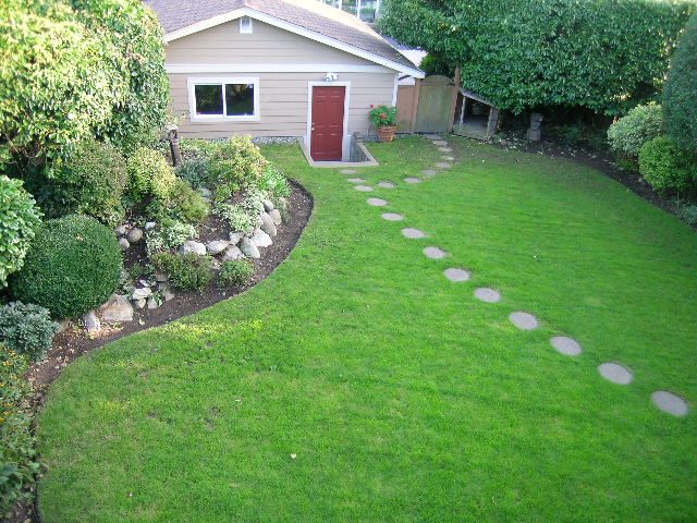 Bright and serene backyard with a red door and stepping stones leading to a garden area. - 875 Whitchurch Street, North Vancouver