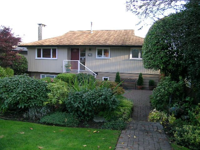 Bright living room with cozy fireplace and large windows, surrounded by lush greenery. - 875 Whitchurch Street, North Vancouver