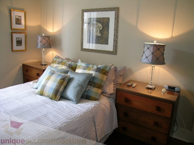 Furnished 1-bedroom condo with cozy bedding, wooden nightstands, and decorative lamps. - 45 - 777 Burrard Street, Vancouver Downtown
