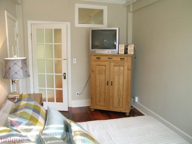 Bright bedroom with hardwood floors, wooden furniture, and a small TV setup. - 45 - 777 Burrard Street, Vancouver Downtown