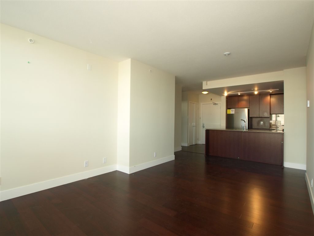 Open living space with hardwood floors and modern kitchen in a bright, empty condo. - 104 - 1320 Chesterfield, North Vancouver