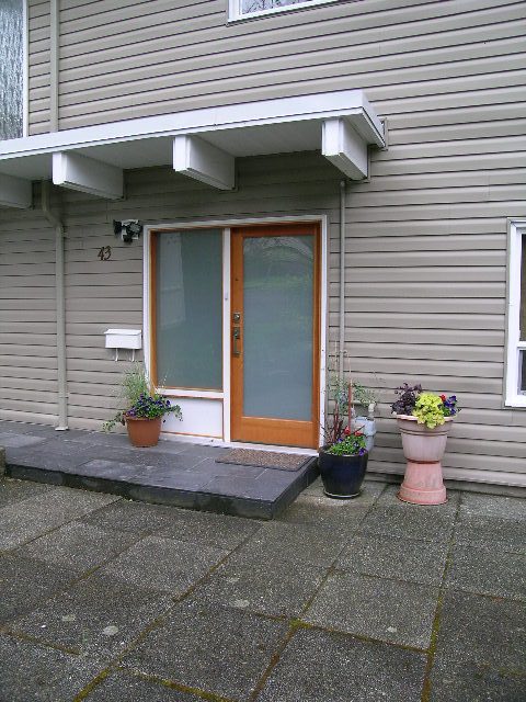 Framed front door with glass panels and a welcoming porch, adorned with potted plants. - 43 Glenmore Drive, West Vancouver