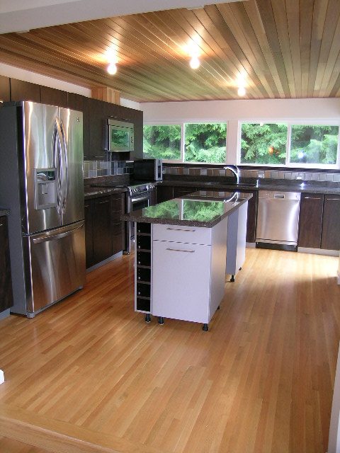 Modern kitchen with stainless steel appliances, hardwood floors, and large windows offering a view of greenery. - 43 Glenmore Drive, West Vancouver