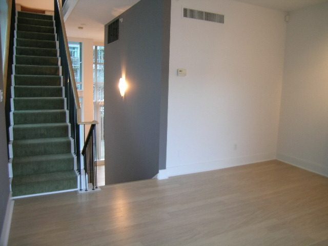 Spacious living room with hardwood floors, green carpeted staircase, and modern lighting. - 1455 West Hastings, Vancouver Downtown