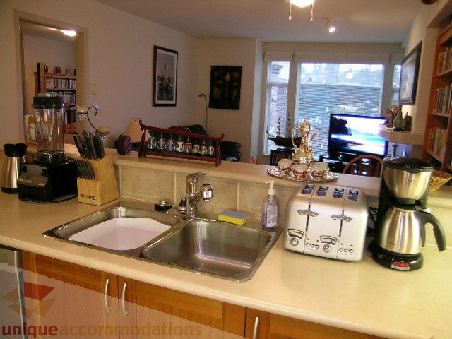 Bright kitchen with stainless steel sink, wooden cabinets, and a cozy corner desk setup. - 215 - 3727 West 10th Avenue, Vancouver West Side