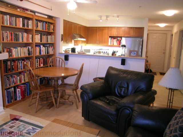 Spacious living room with leather couch, bookshelf, and kitchen in the background. - 215 - 3727 West 10th Avenue, Vancouver West Side