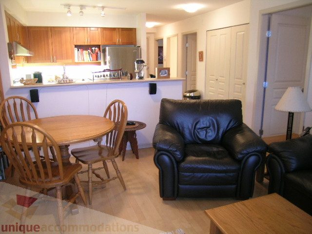 Furnished living room with black leather couches and wooden dining table, hardwood floors, and kitchen counter in the...