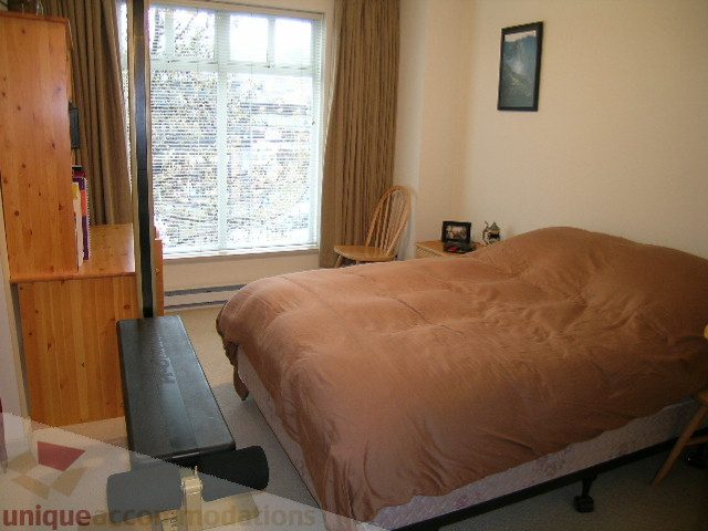Spacious bedroom with large window, wooden furniture, and cozy bedding. - 215 - 3727 West 10th Avenue, Vancouver West Side