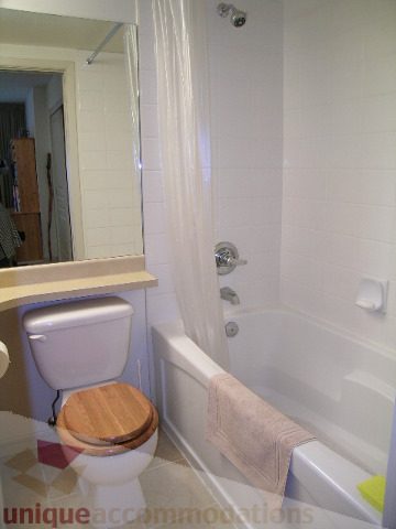 Bathroom with white fixtures, wooden toilet seat, and towel hanging on tub. - 215 - 3727 West 10th Avenue, Vancouver West Side