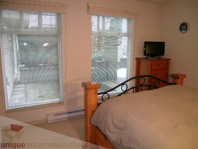 Spacious bedroom with large windows, wooden headboard, and a flat-screen TV on a wooden dresser. - 215 - 3727 West 10th Avenue, Vancouver West Side