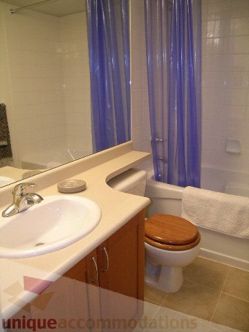 Modern bathroom with white countertop, wooden toilet seat, and blue shower curtain. - 215 - 3727 West 10th Avenue, Vancouver West Side