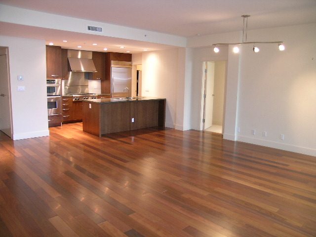 Open-concept living space with hardwood floors and a modern kitchen featuring stainless steel appliances and dark wood...