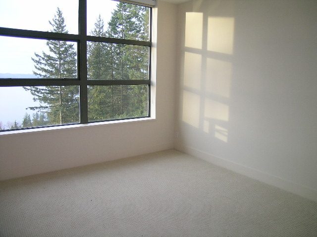 Bright living room with large windows, offering a view of trees and a serene outdoor space. - 602 - 3355 Cypress Place, West Vancouver