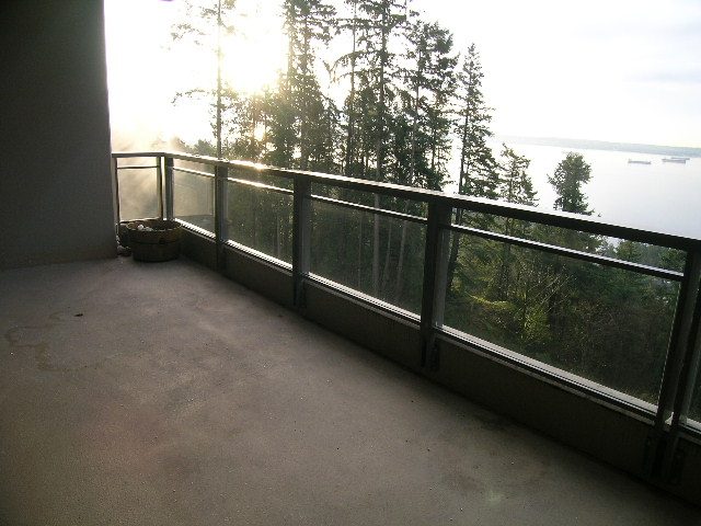 Furnished balcony with a view of trees and water, featuring a glass railing and concrete flooring. - 602 - 3355 Cypress Place, West Vancouver
