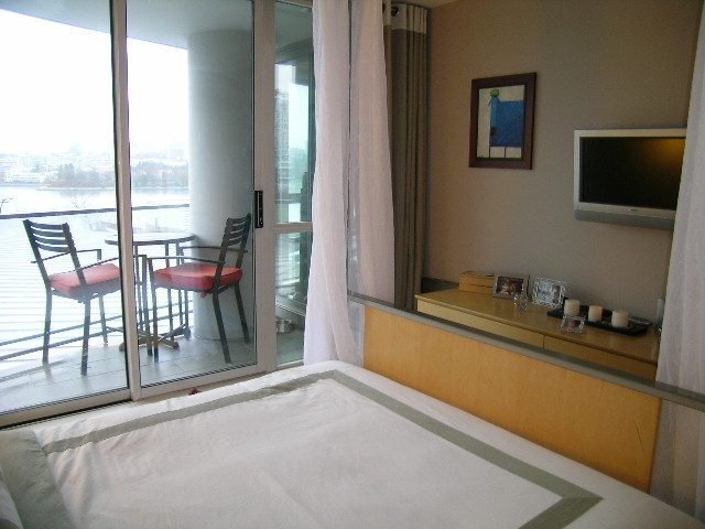 Spacious bedroom with large windows offering a city view, neatly made bed, and wooden headboard. - 508 - 1408 Strathmore Mews, Vancouver Downtown