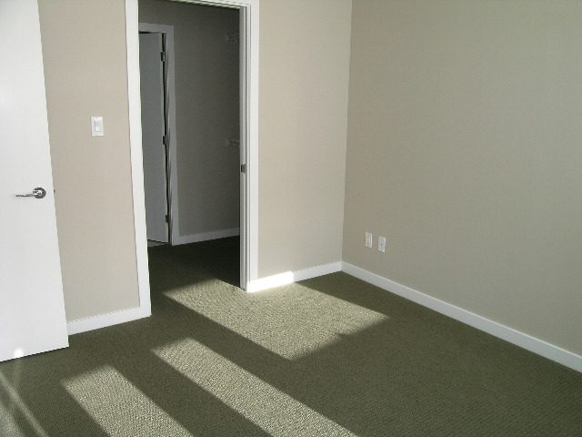 Spacious 1-bedroom condo with neutral walls and carpeted floors, featuring a cozy corner and natural light.