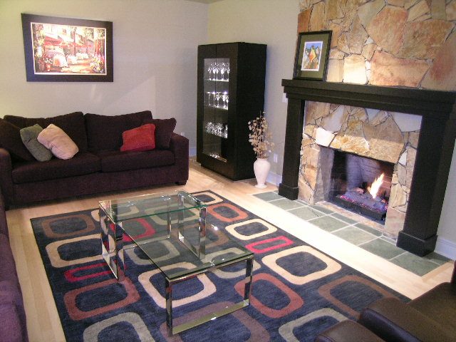 Spacious living room with a cozy fireplace, modern glass coffee table, and vibrant geometric rug. - 3272 Brookridge Drive, North Vancouver
