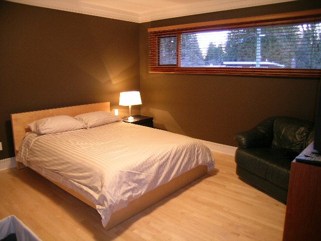 Spacious bedroom with wooden floors, a large bed, and a window with blinds. - 3272 Brookridge Drive, North Vancouver