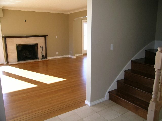 Spacious living room with hardwood floors and a fireplace, leading to a staircase. - 1875 26th Street, West Vancouver