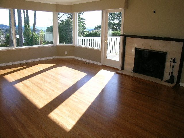 Spacious living room with hardwood floors, large windows, and a fireplace, offering a serene view of the outdoors. - 1875 26th Street, West Vancouver