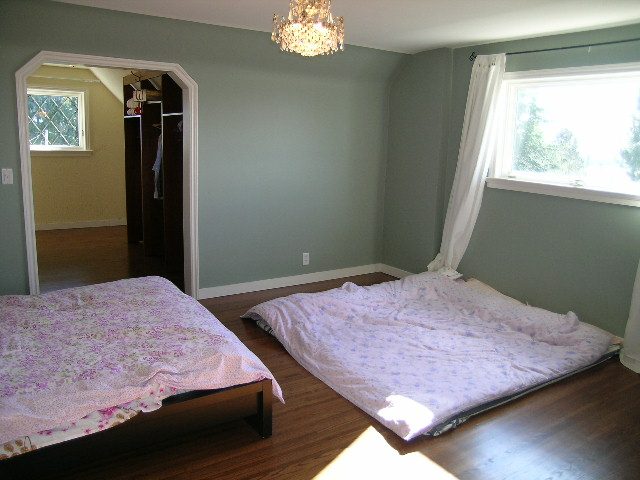 Spacious bedroom with hardwood floors and a large window, featuring a neatly made bed with floral bedding. - 1875 26th Street, West Vancouver
